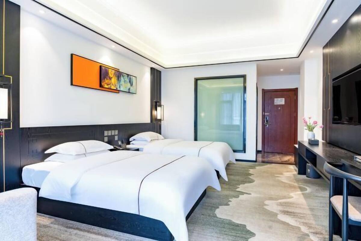 Una habitación de hotel moderna con dos camas, un televisor de pantalla plana, un cuadro en la pared y una puerta que da a otra habitación.