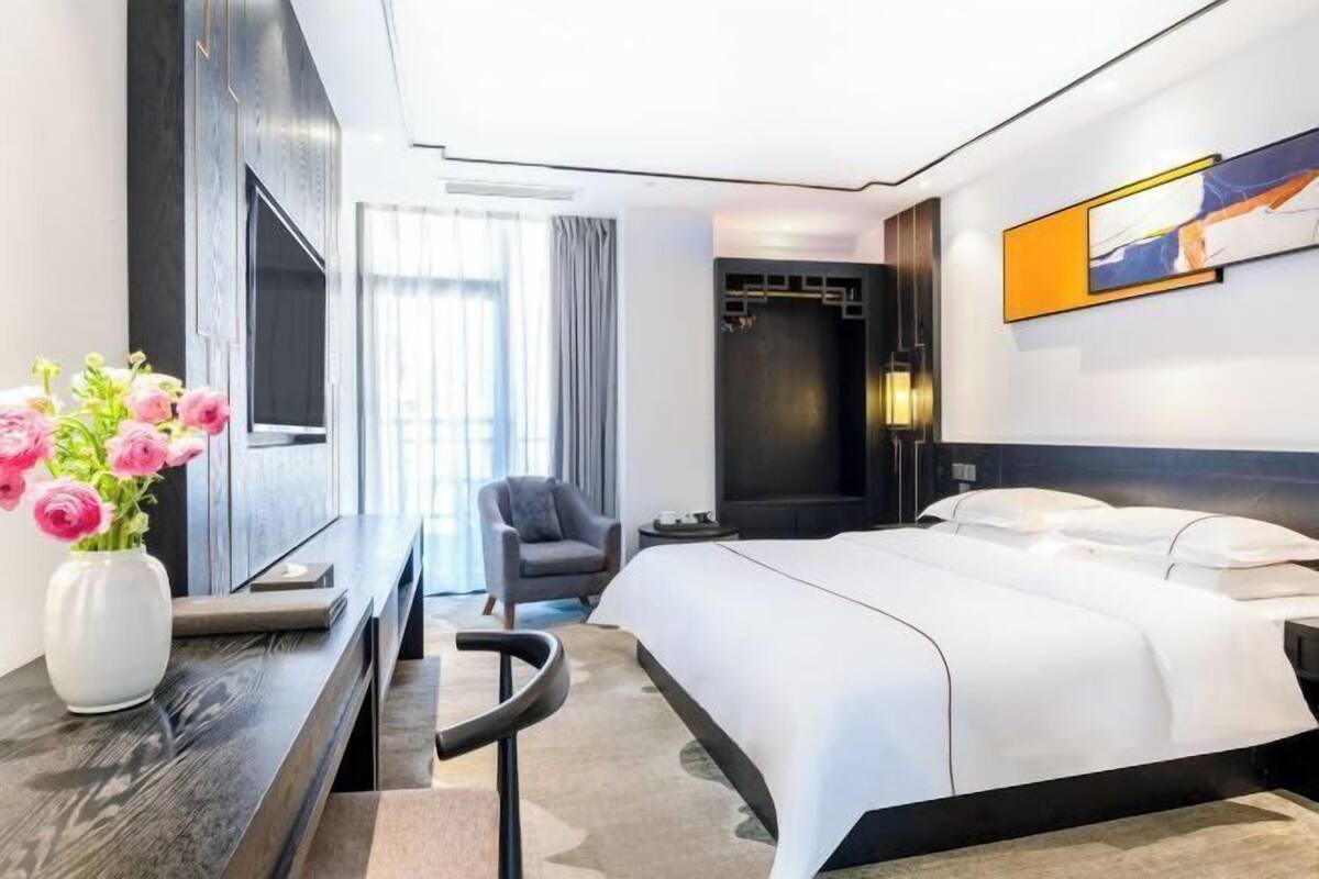 Una habitación de hotel moderna con una cama grande, un escritorio, una silla, un televisor y una obra de arte colgada en la pared.