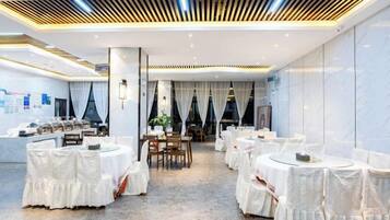 A spacious banquet hall with round tables and chairs, a central dining area, and a modern ceiling design.