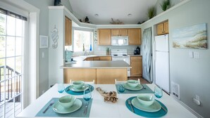 Una cocina moderna con una isla central, armarios de madera y un comedor preparado para cuatro, con individuales y cuencos color aguamarina.