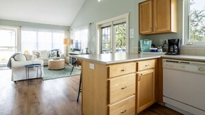 Un salón comedor amplio con cocina, armarios de madera y ventanas grandes.