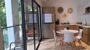 Et moderne køkken med indbygget ovn, et rustfrit stål køleskab og et spiseområde med et rundt bord og hvide stole.