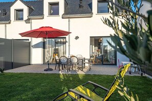 A modern house with a patio area featuring a red umbrella, outdoor seating, and a well-maintained lawn.