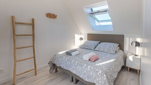 Une chambre avec une lucarne, une échelle en bois, un lit avec une literie à motifs et des lampes de chevet.