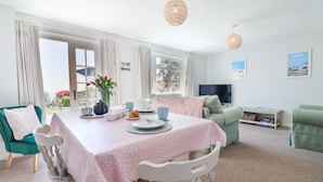 A dining area with a table set for two, a green armchair, and a television in the background. - The Seaside Inn (Seaton)