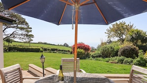 A round wooden table with two chairs, an umbrella, and a bottle of wine. - The Seaside Inn (Seaton)