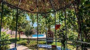 Un espace extérieur abrité, avec une table dressée pour deux, une piscine en arrière-plan et une végétation luxuriante.