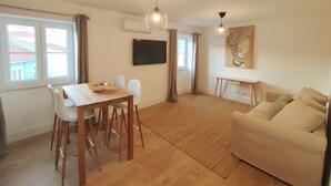 A modern living room with a wooden dining table, white chairs, a beige sofa, and a large painting on the wall. - Lisbon Skyline Apartment by Misha s Place 5E (Lisbon)