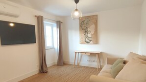A living room with a sofa, a TV mounted on the wall, a desk, and a painting. - Lisbon Skyline Apartment by Misha s Place 5E (Lisbon)