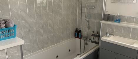 A modern bathroom with a marble wall, a bathtub, a shower, and a sink.