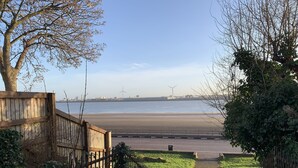 Vista de uma praia com uma cerca e uma área gramada em primeiro plano.