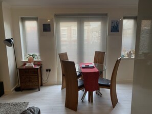 Ein Essbereich mit einem Glastisch, Holzsesseln und einer roten Tischläufer. Dort steht ein Schreibtisch mit einer Lampe und einer Pflanze.