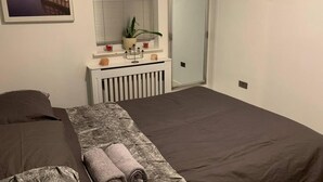 Quarto com uma cama, mesa de cabeceira com uma planta, radiador e janela com persianas.