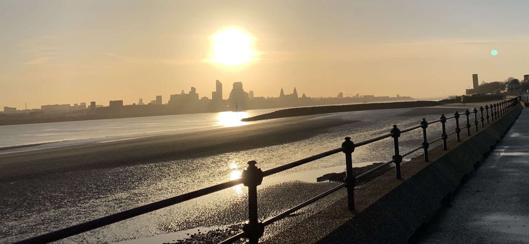 A coastal cityscape at sunset with a waterfront promenade.