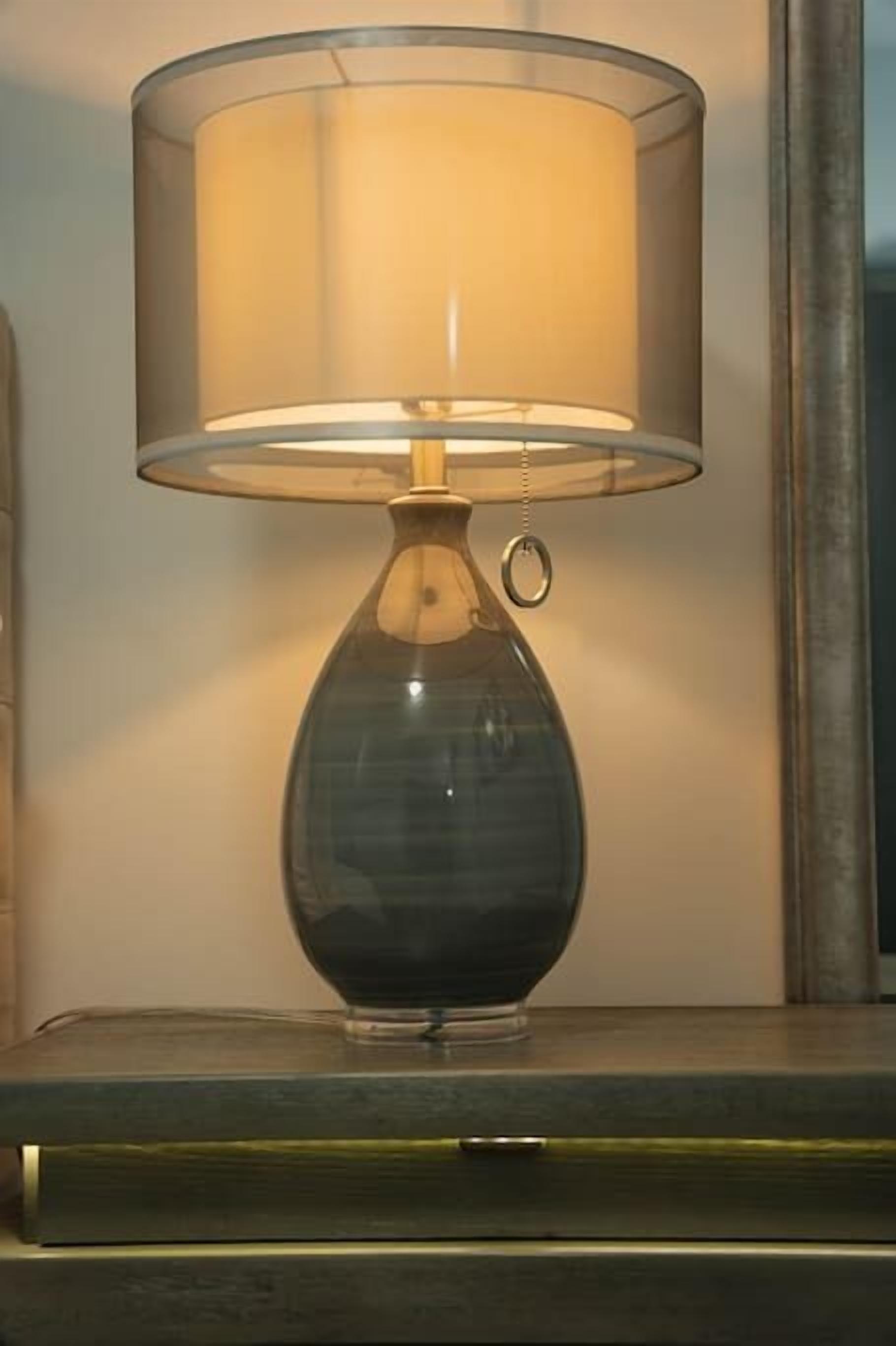 Eine Tischlampe mit einem klaren Glasenschirm und einem Metallfuß, platziert auf einer Holzfläche.