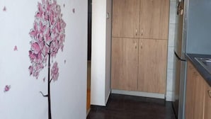 A kitchen with wooden cabinets, a refrigerator, and a wall with a floral decal. - Stunning Color 1-bed Apartment in Skopje (Skopje)