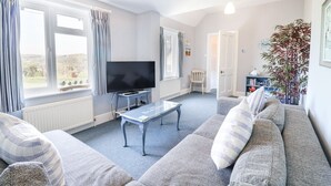 A living room with a sofa, a TV, a table, and a bookshelf. - The Boat Shed (Seaton)