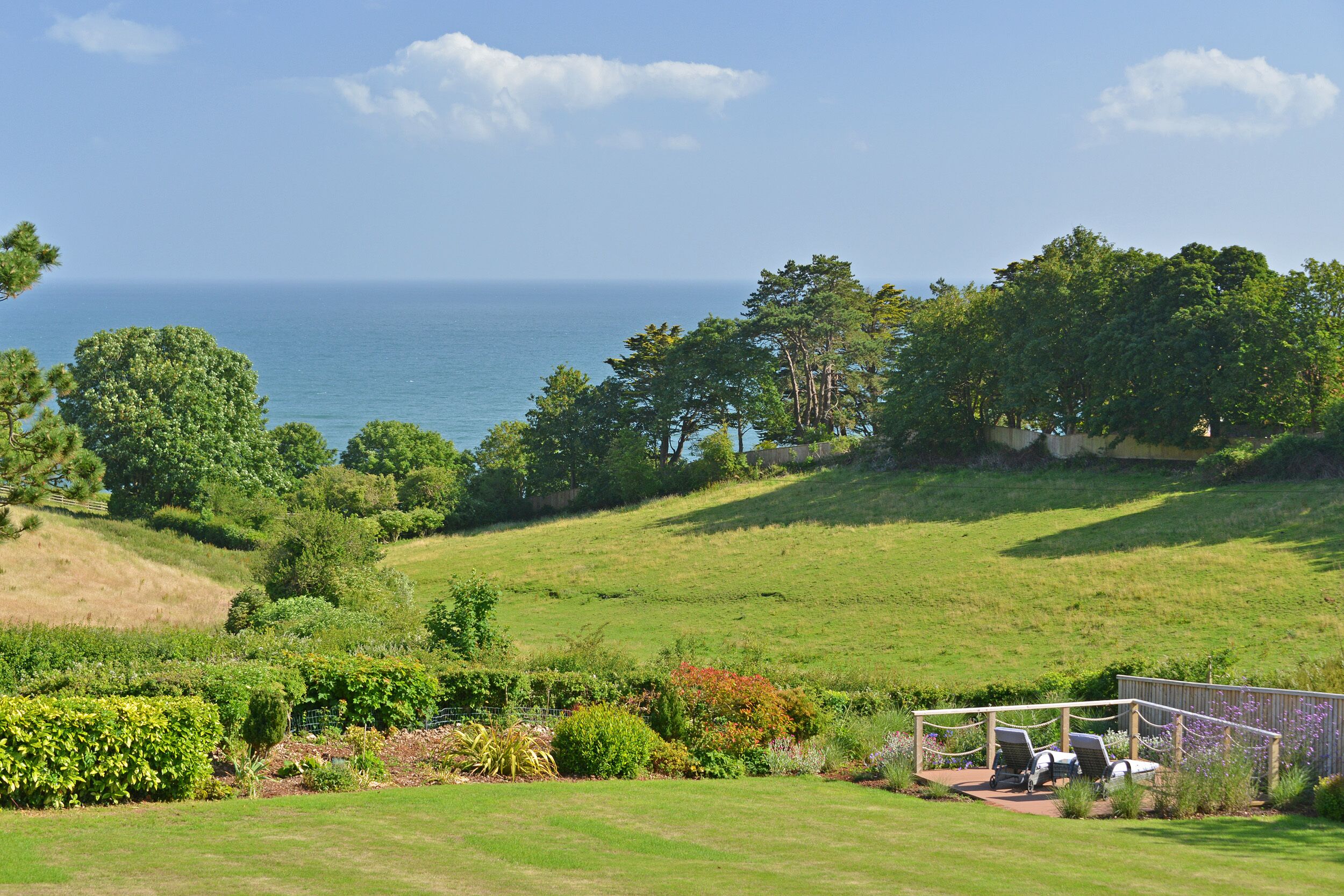 A lush green landscape with a view of the ocean, a gazebo with seating, and a variety of trees and shrubs.
