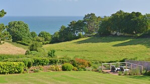 A lush green landscape with a view of the ocean, a gazebo with seating, and a variety of trees and shrubs. - The Boat Shed (Seaton)