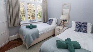 A hotel room with two beds, a nightstand, a lamp, a mirror, and a window with curtains. - The Boat Shed (Seaton)
