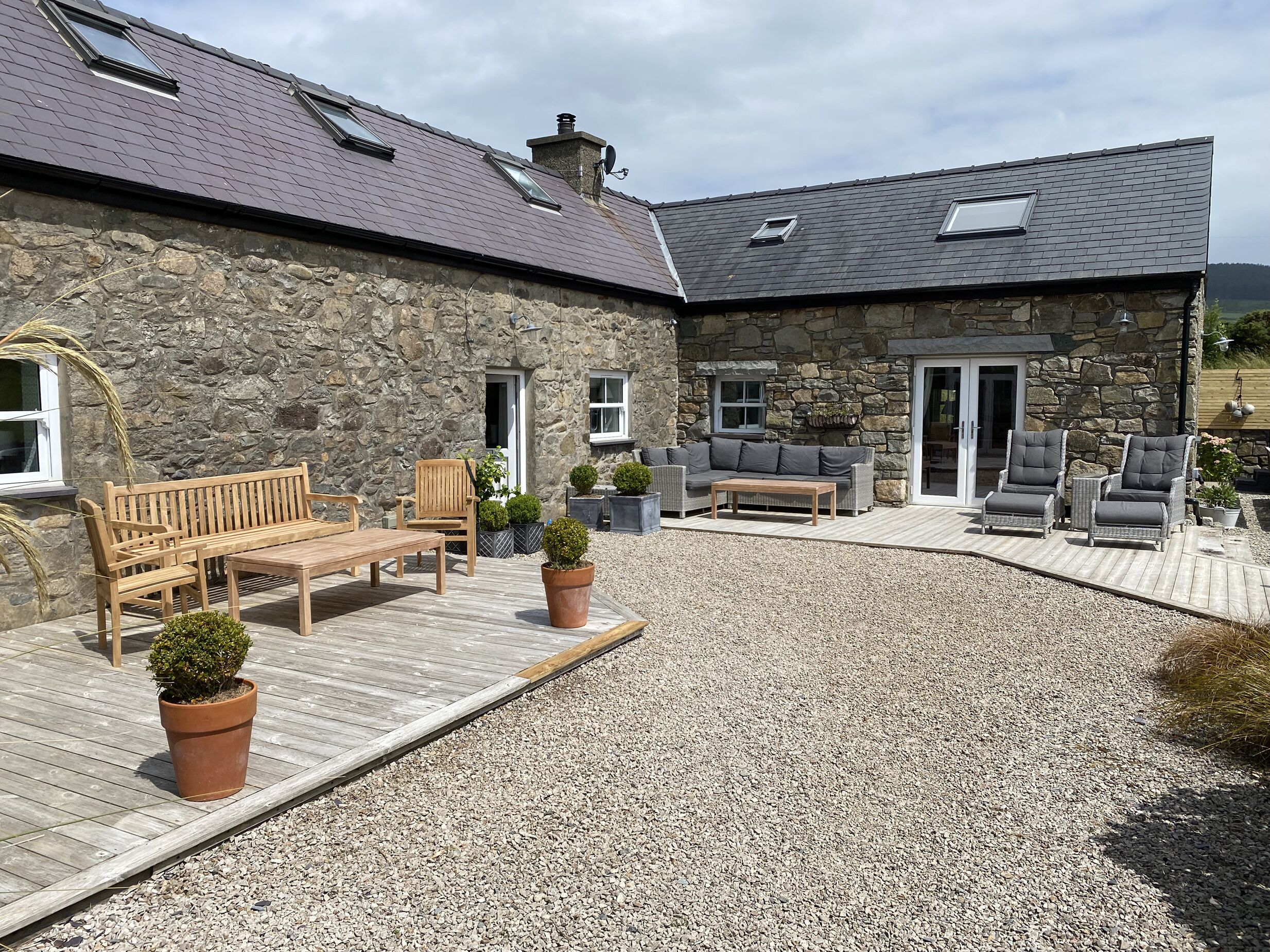 Un bâtiment en pierre doté d’un patio aménagé avec des meubles d’extérieur, une terrasse en bois et des plantes en pot.