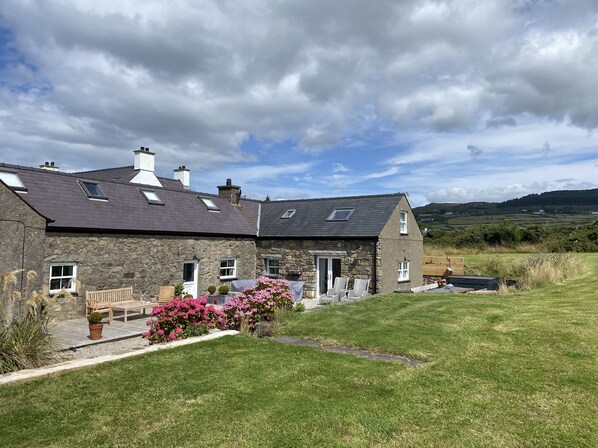 A stone house with a sloped roof, multiple windows, and a small porch with outdoor seating.