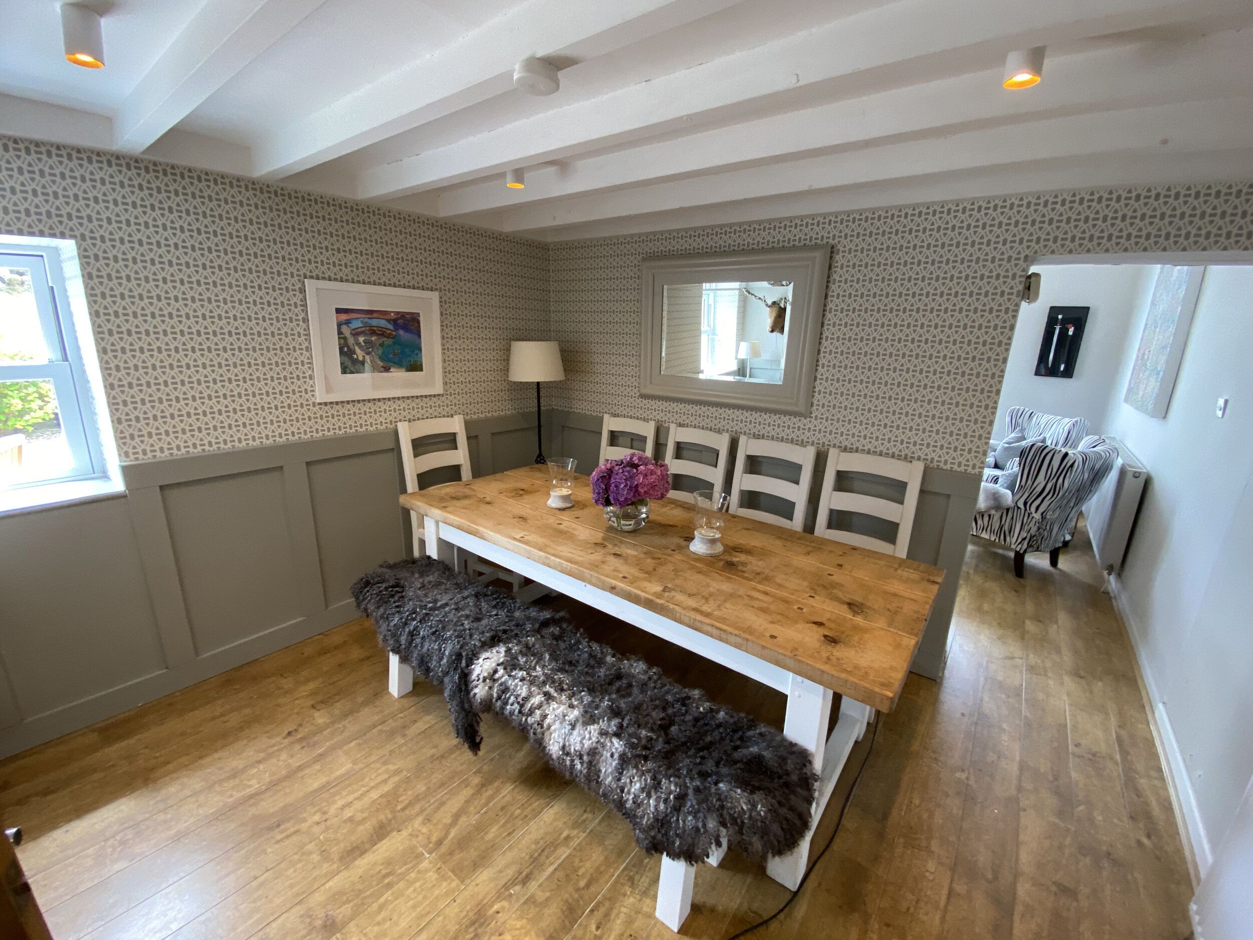 A dining area with a wooden table, white chairs, a bench, and a patterned wall.