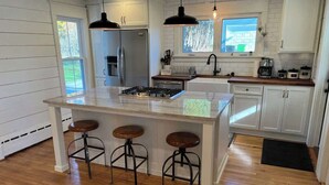 Una cocina con una isla central, taburetes de bar, un refrigerador, un lavamanos y una ventana.