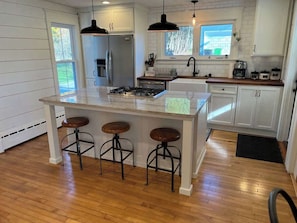 A kitchen with a central island, bar stools, a refrigerator, a sink, and a window.