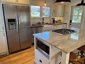 A modern kitchen with a stainless steel refrigerator, a built-in oven, a gas stove, and a marble countertop. - Modern Farmhouse with Porch near Lake & Downtown (Green Lake)