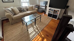 Una sala de estar con sofá, mesa de centro de vidrio, televisor y estantería.