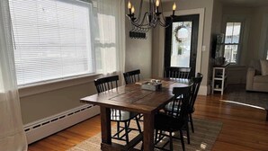 Un comedor con una mesa de madera, sillas, una araña y vistas a través de un ventanal.