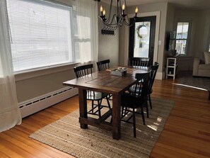 A dining area with a wooden table, chairs, a chandelier, and a view through a window.