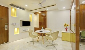 A modern conference room with a round table, four chairs, a flat-screen TV, and a small cabinet with a vase of sunflowers. - Treebo Jannat Residency (New Delhi)