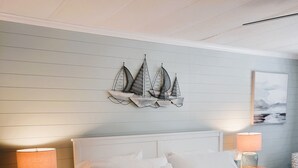 Een netjes opgemaakt slaapkamer met een groot bed, twee nachtkastjes met lampen, een schip aan de wand en een ingelijste foto.