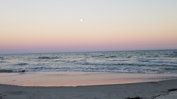 A beach with waves and a crescent moon in the sky.