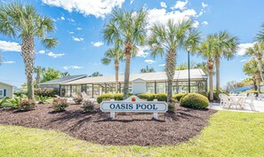 A sign for Oasis Pool surrounded by palm trees and a building with a glass facade.