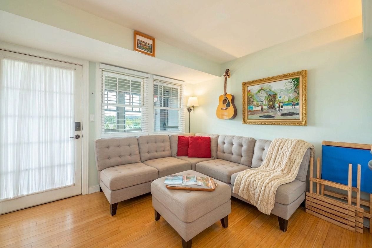 A living room with a sectional sofa, a coffee table, a guitar, and a painting on the wall.