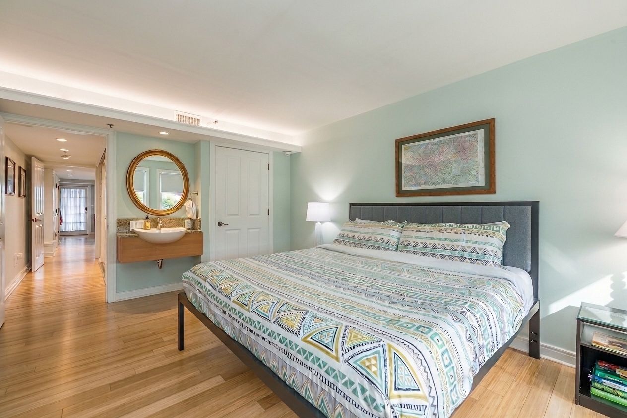 A bedroom with a bed, a bedside table, a nightstand, a mirror, a window, and a door.
