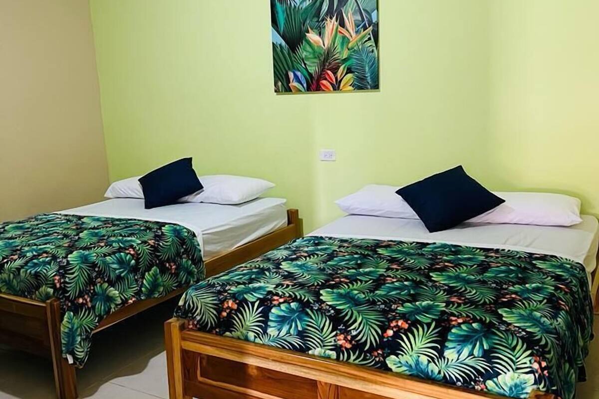 A room with two wooden beds, each with a tropical leaf-patterned bedspread and pillows.