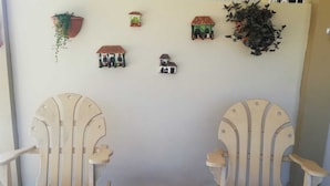 Two wooden chairs with curved backs and armrests, a small wooden table with a tree stump center, and several small decorative houses on the wall. - Villas Don Pablo (Las Tablas)