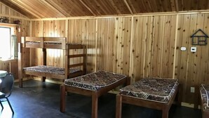 Interior d'una cabana de fusta amb lliteres, una taula de menjador i una cuina petita.