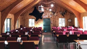Una sala espaiosa amb revestiment de fusta, un sostre alt i una figura d'animal negre al centre. Taules i cadires disposades per seure.
