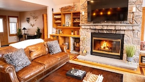 Una sala de estar acogedora con chimenea de piedra, sofá de cuero y televisor de pantalla plana montado encima.