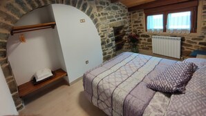 A bedroom with a stone wall, a bed with patterned bedding, a wooden ceiling, and a window with curtains. - Apartment for two adults and two children ski Formigal Panticosa VTT (Senegüé)
