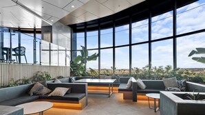 Un área de descanso moderna con asientos, una mesa y ventanas amplias que ofrecen vistas de la ciudad.