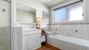 A bathroom with a large mirror, a bathtub, a sink, and a window. - Serenity Now Inverloch (Inverloch)