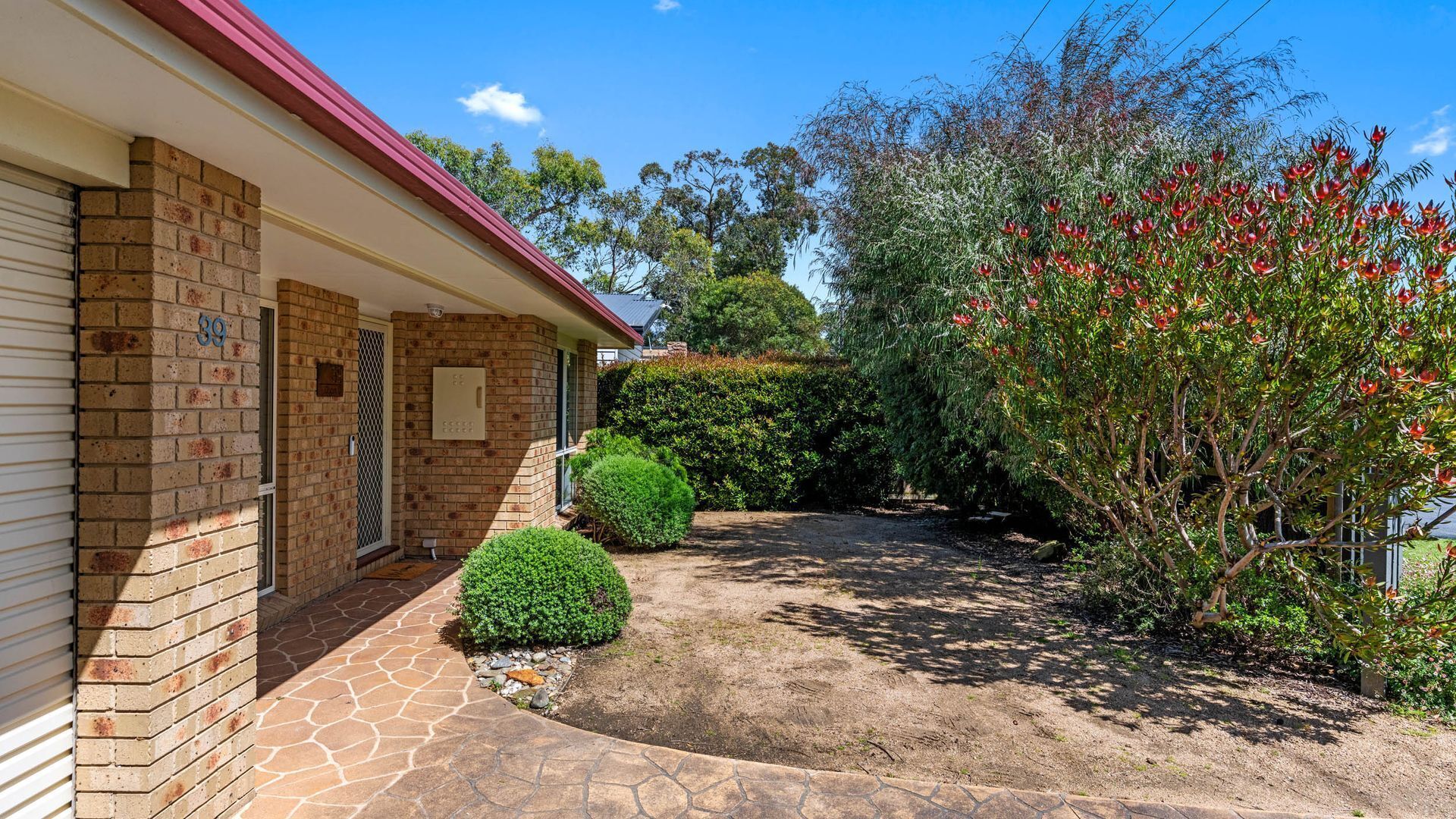 A brick house with a number '39' on the wall, a small front yard with a paved path, and a flowering bush.