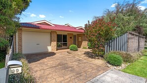 A residential house with a red-tiled roof, a garage, and a paved driveway leading to the front door. - Serenity Now Inverloch (Inverloch)