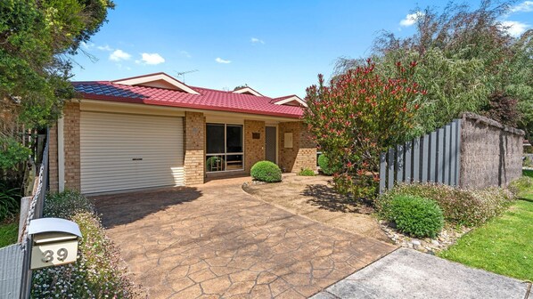 A residential house with a red-tiled roof, a garage, and a paved driveway leading to the front door. - Serenity Now Inverloch (Inverloch)